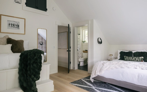 Upstairs bedroom featuring sloped ceiling, king bed with textured throw, patterned accent wall, and natural wood dresser